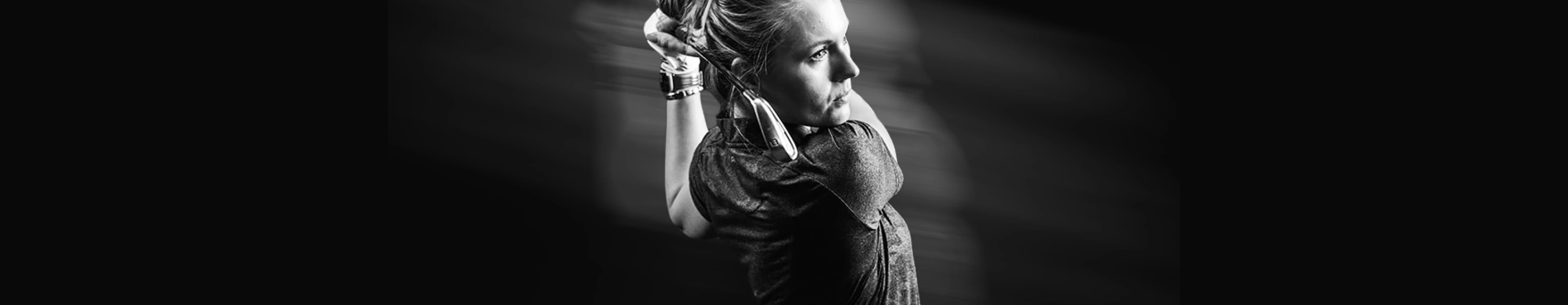 Black and white image of a person in motion, holding a golf club behind their head, looking focused with a blurred background.