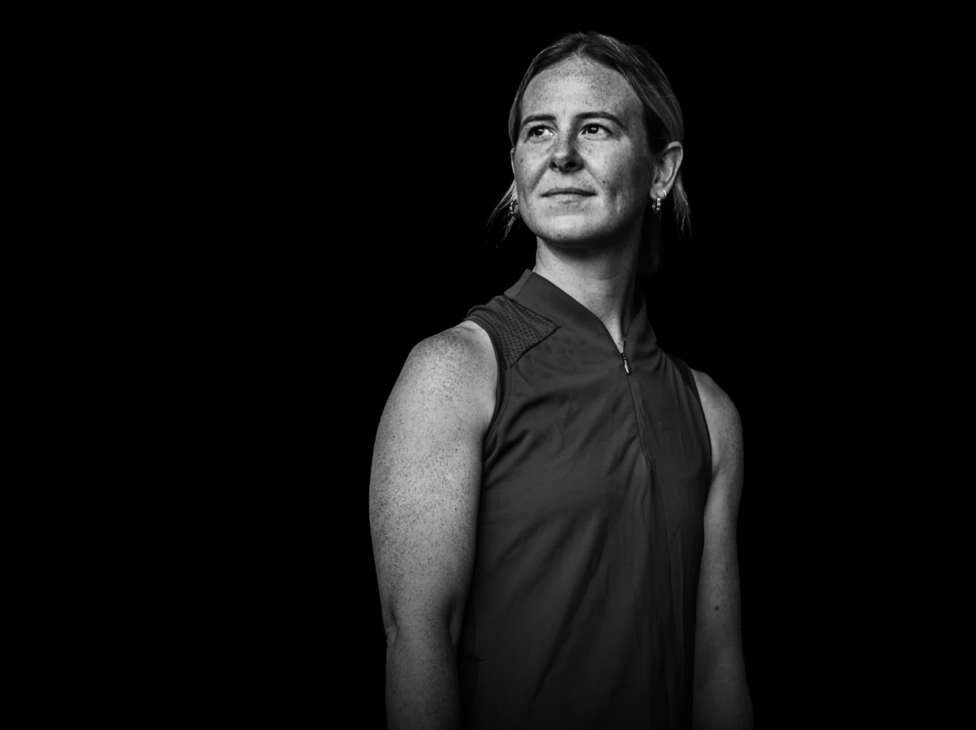 Black and white portrait of a person with short hair, wearing a sleeveless top, looking confidently to the side.