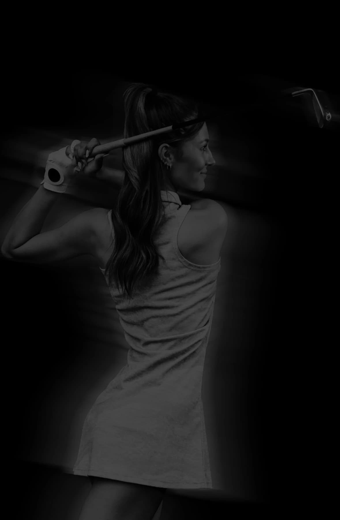 A woman in a sleeveless dress holds a golf club, posing with a confident smile. She wears a ponytail and a glove on one hand.